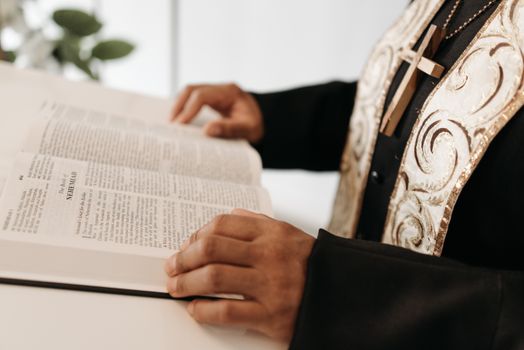 A pastor reads an open Bible, wearing religious attire with a cross necklace.
